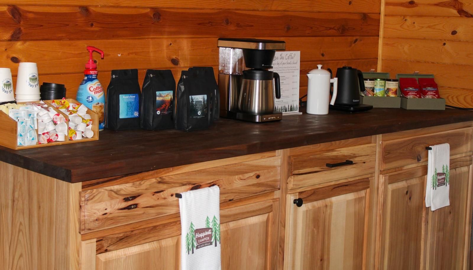 Kitchen counter with coffee maker, mugs, and coffee supplies against a wood-paneled wall.