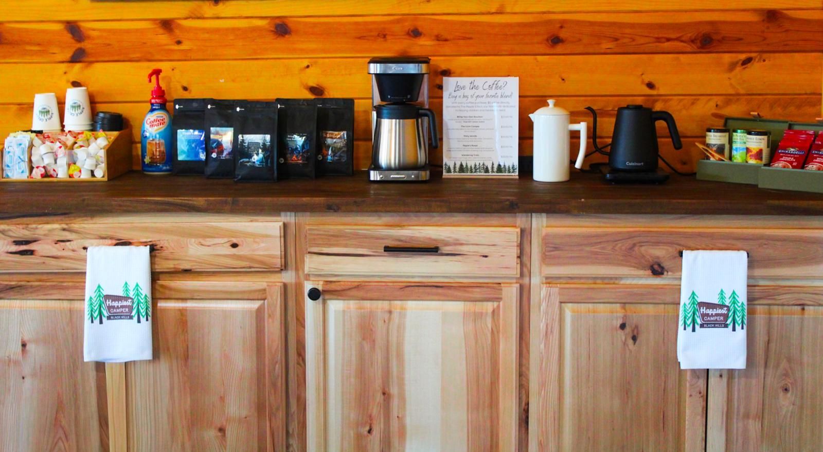 Wooden coffee bar with coffee maker, mugs, jars, and a black kettle on a rustic countertop.