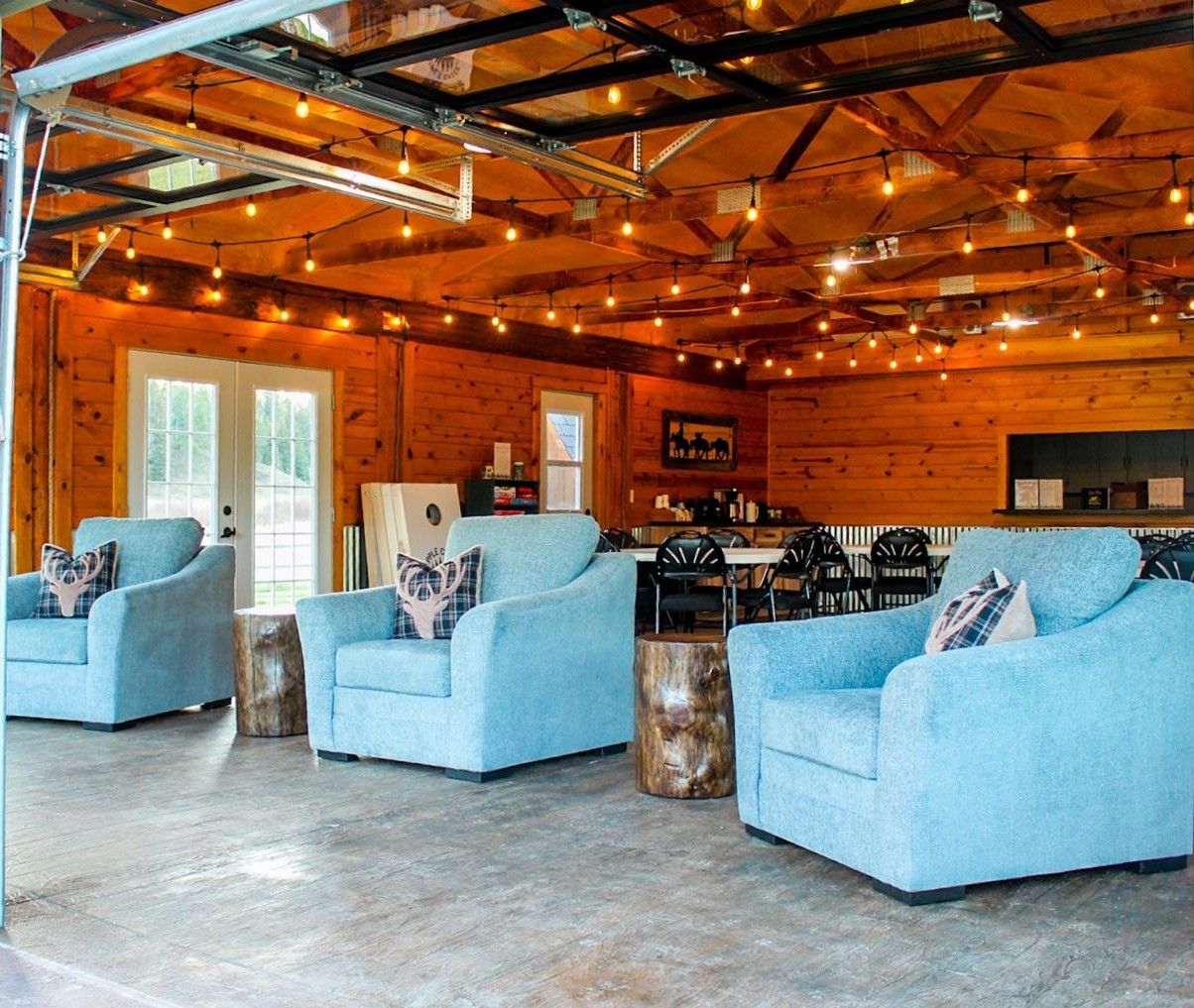 Rustic lounge with blue armchairs, wooden walls, string lights, and exposed ceiling beams