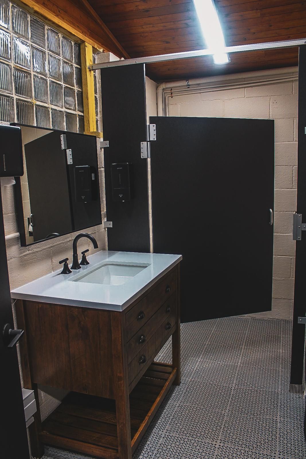 Small rustic restroom with a wood sink cabinet, black stall door, and patterned floor.