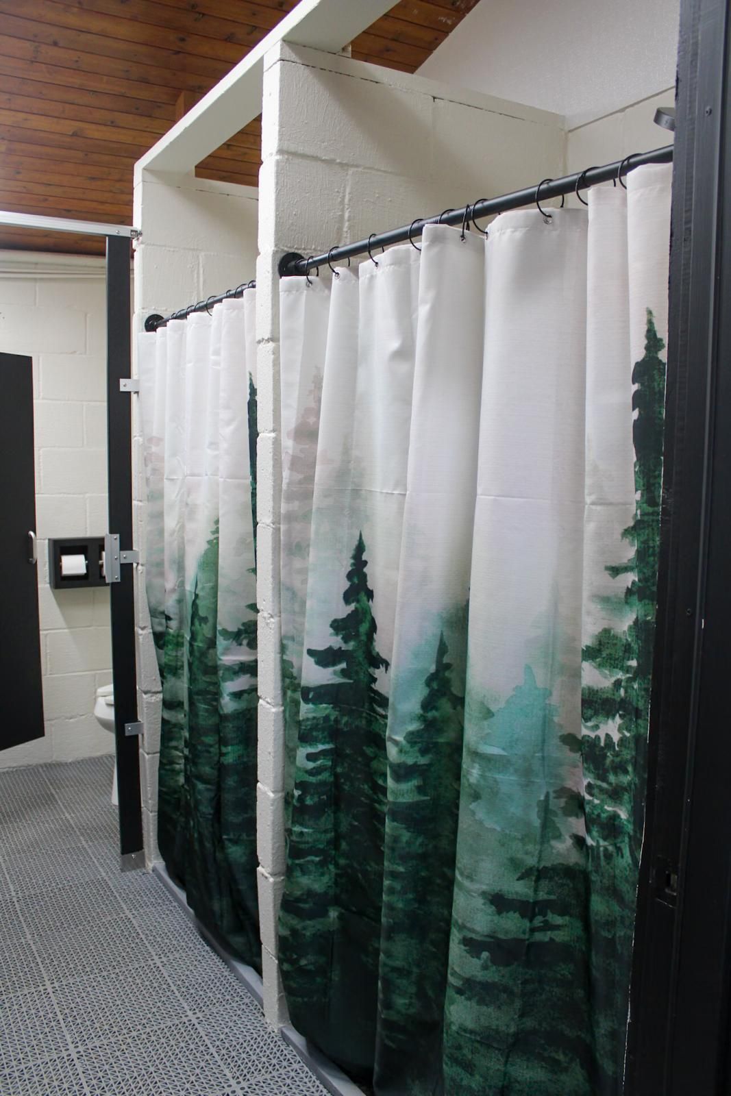 White forest-print shower curtains in a row of bathroom stalls along a carpeted hallway