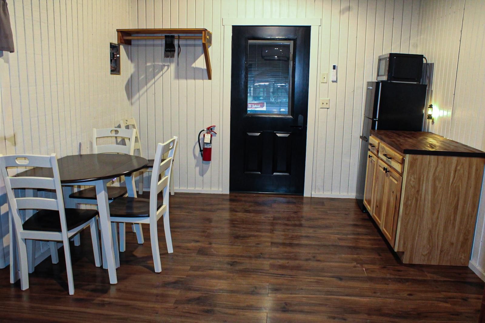 Small dining area with table and chairs, black door, and wooden cabinet along the wall.
