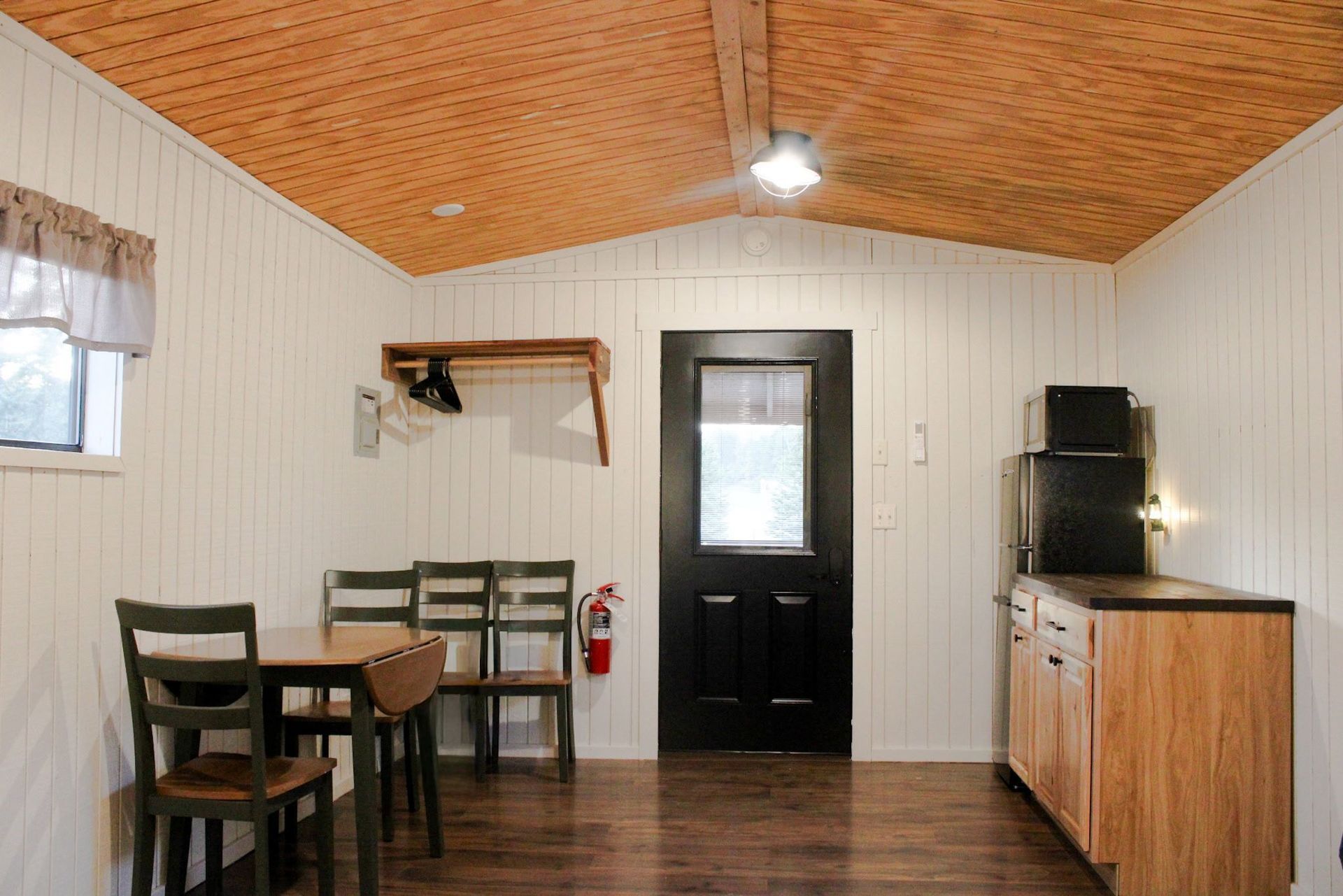 Small dining area with wood ceiling, black door, table, chairs, and a cabinet against the wall.