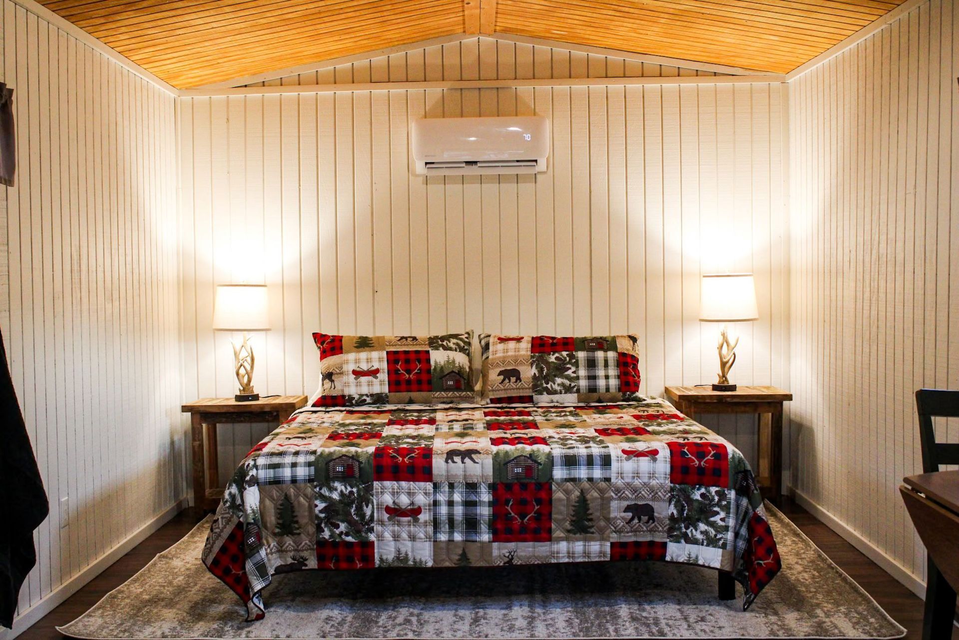 Cozy bedroom with a patterned bedspread, twin lamps, air conditioner, and wood-paneled walls