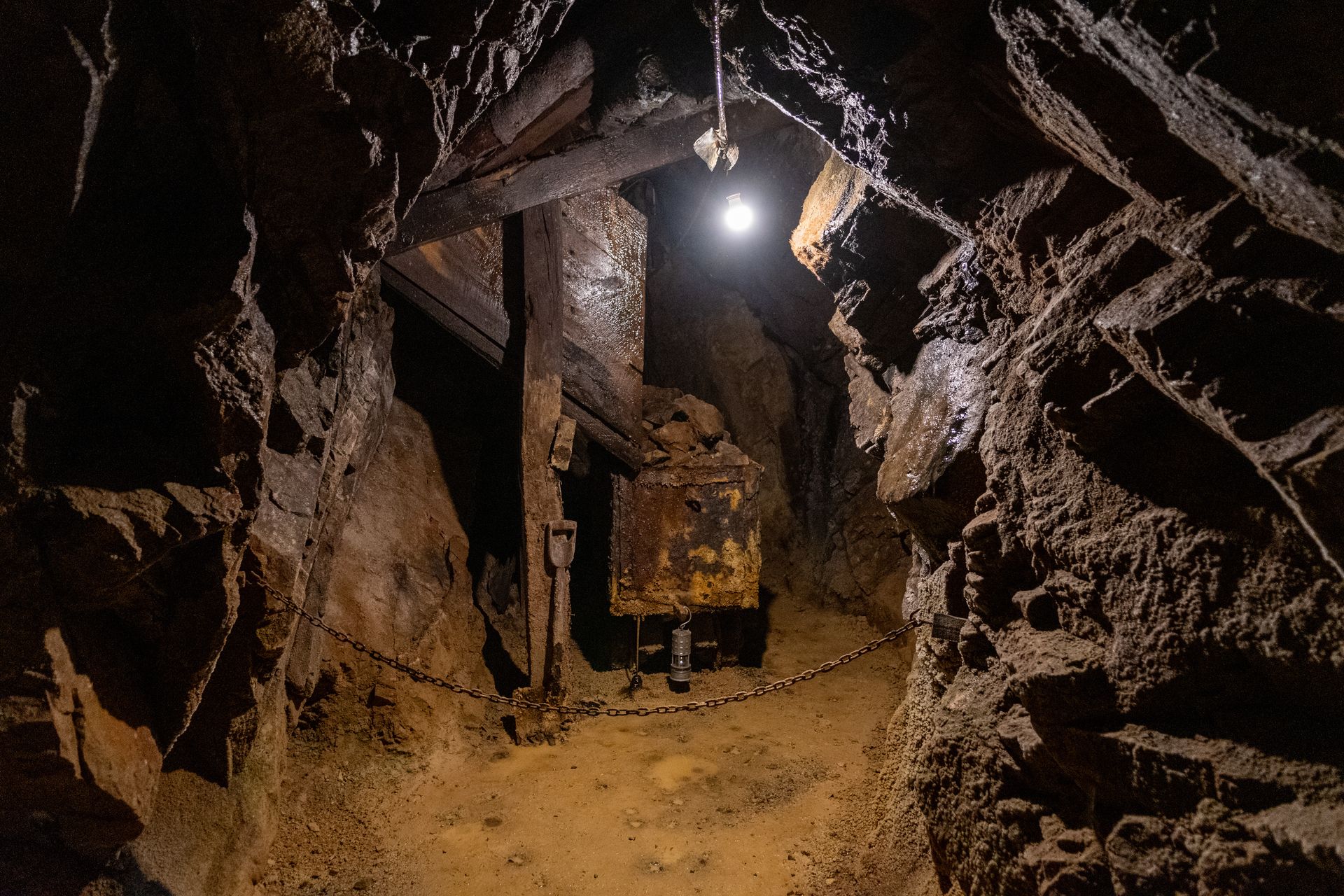 Narrow underground mine tunnel with wooden supports and a bright lamp illuminating rough rock walls