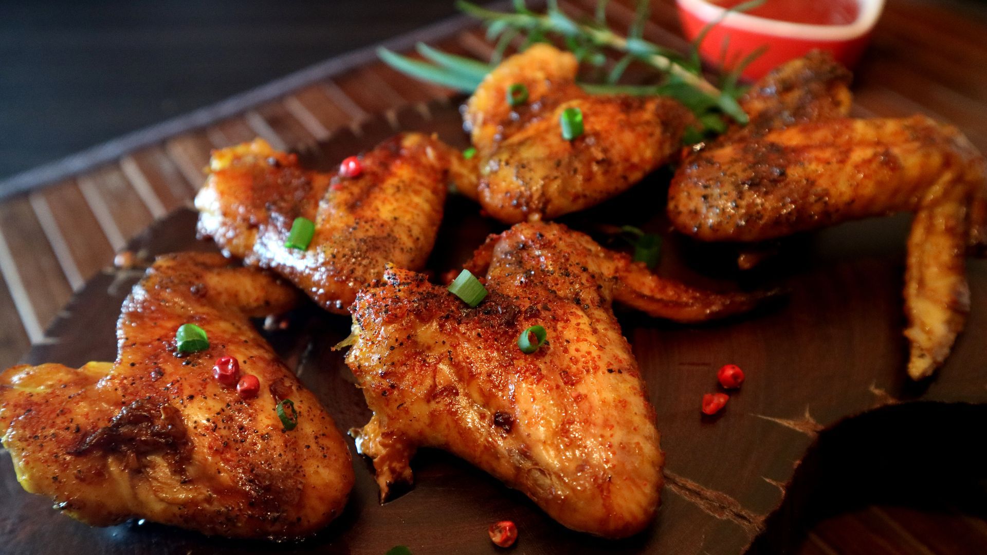 Plate of glazed chicken wings with herbs and chili flakes on a dark serving board