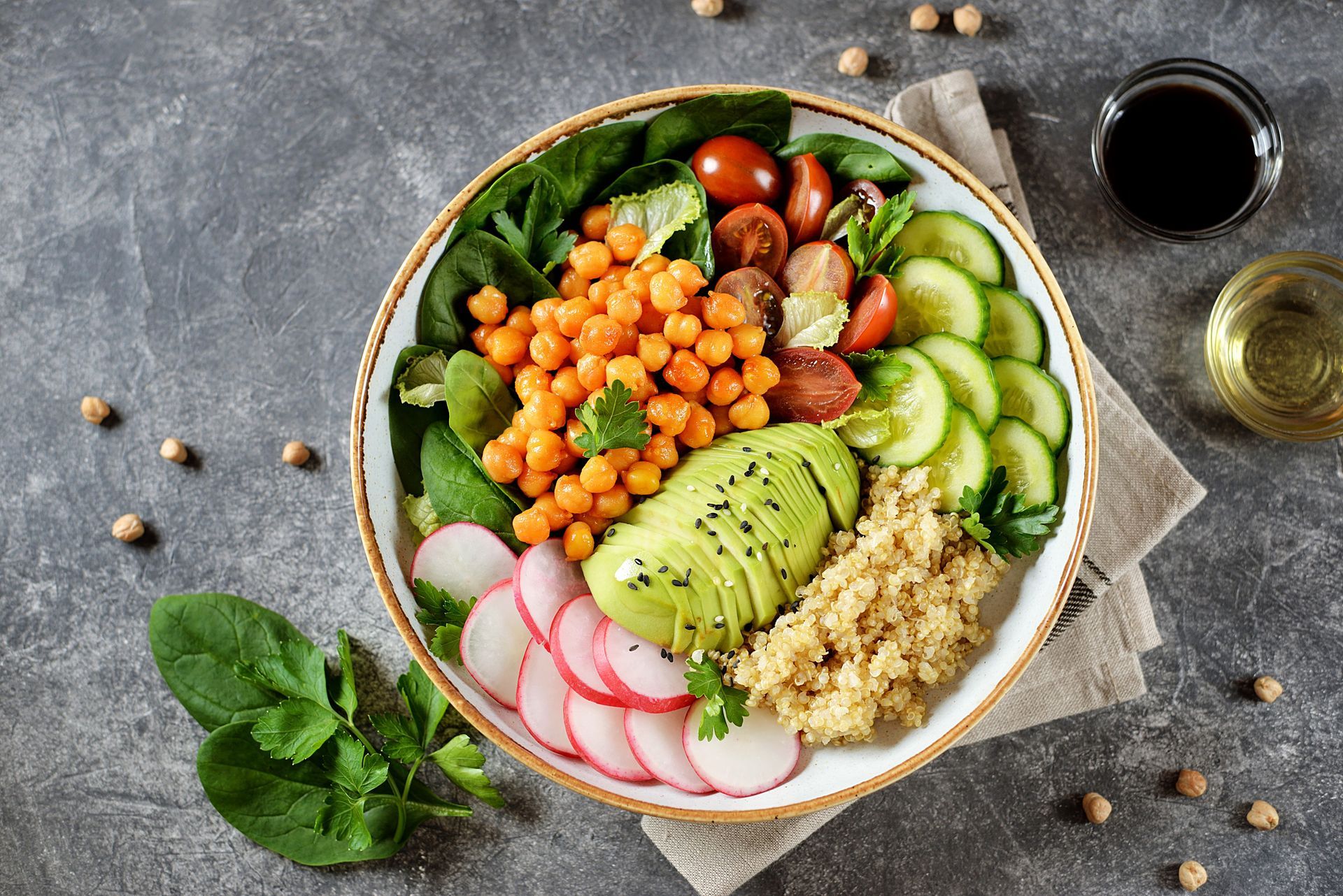 Colorful poke bowl with avocado, cucumber, radish, chickpeas, greens, and grains on a gray table