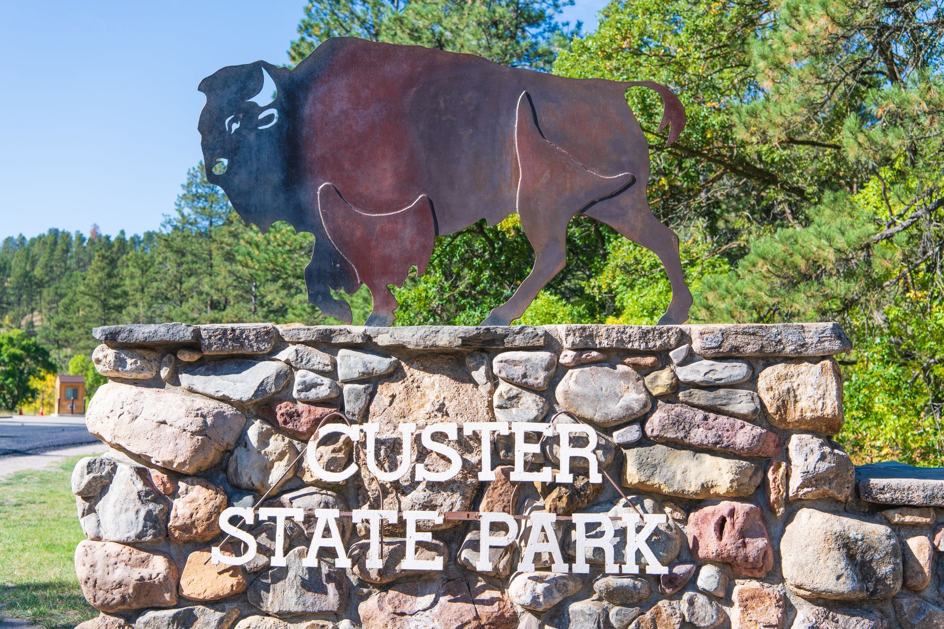 Bison statue atop a stone sign reading “CUSTER STATE PARK” under a blue sky