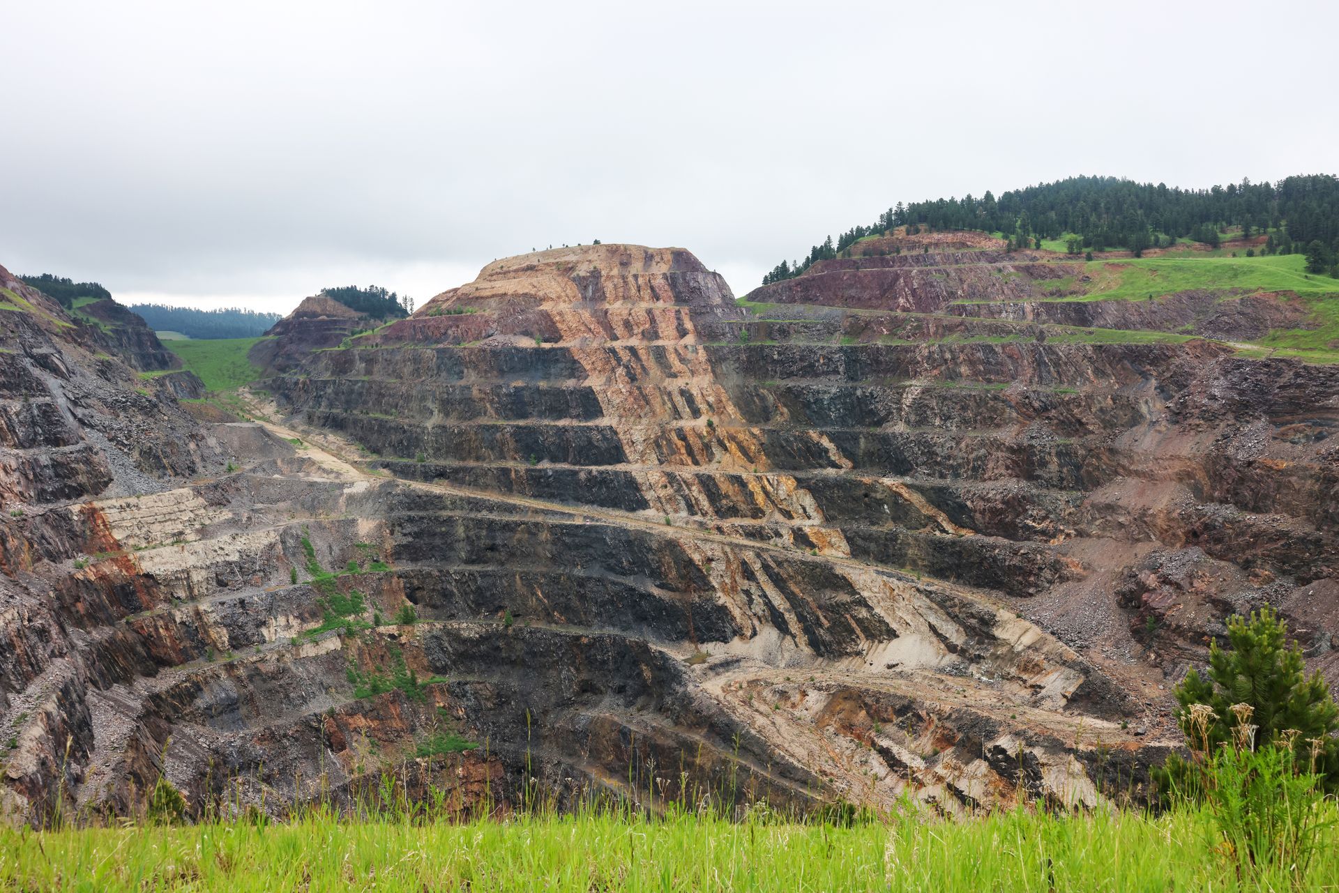 Terraced open-pit mine with exposed rock layers and green hills in the background