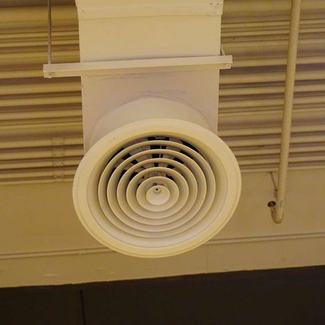 A white air vent is hanging from the ceiling of a building.