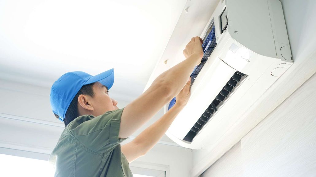 A man in a blue hat is fixing an air conditioner.