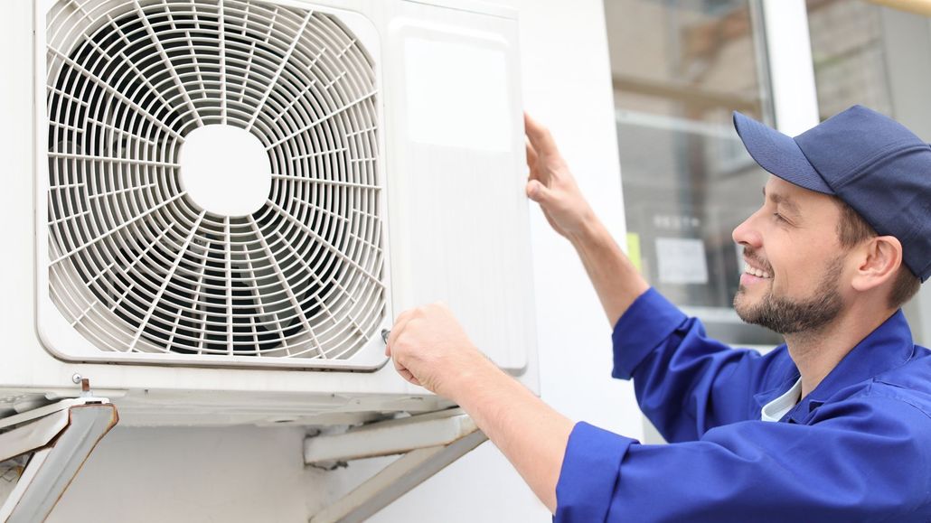 A man is fixing an air conditioner on the side of a building.