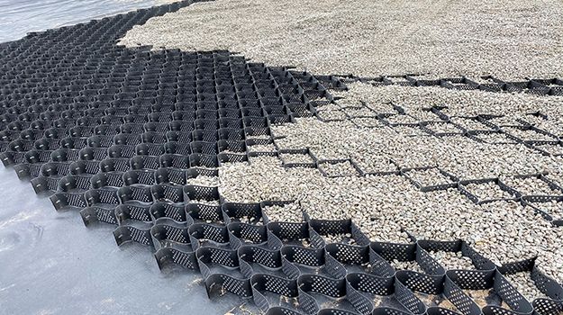 Black plastic grid paving over light gravel, partly covered by snow along the edge.