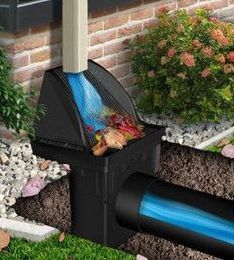 Rainwater diverter directing blue water from a downspout into an underground pipe next to a brick wall