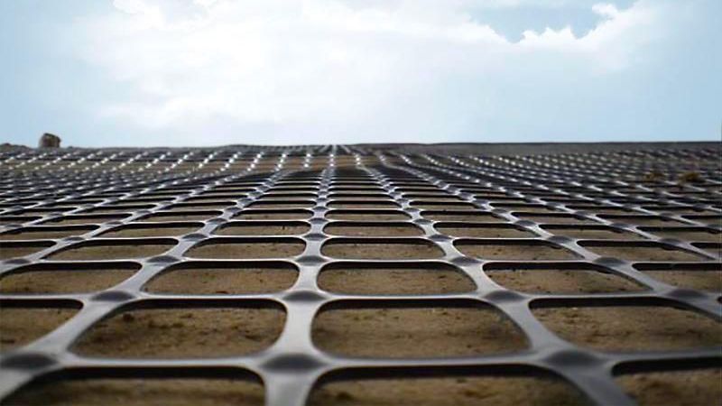 Low-angle view of a perforated metal grid against a blue sky with clouds