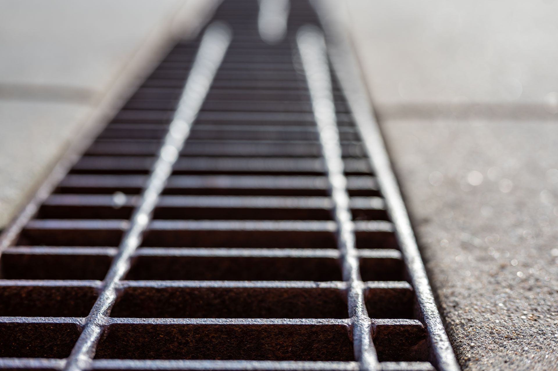 Close-up of a metal storm drain grate in pavement, viewed from ground level