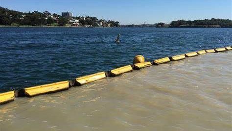Yellow floating barrier separating muddy and blue water on a river, with shoreline in the distance.