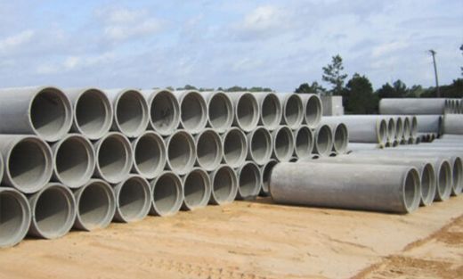 Stacks of large gray concrete pipes stored outdoors on a sandy lot