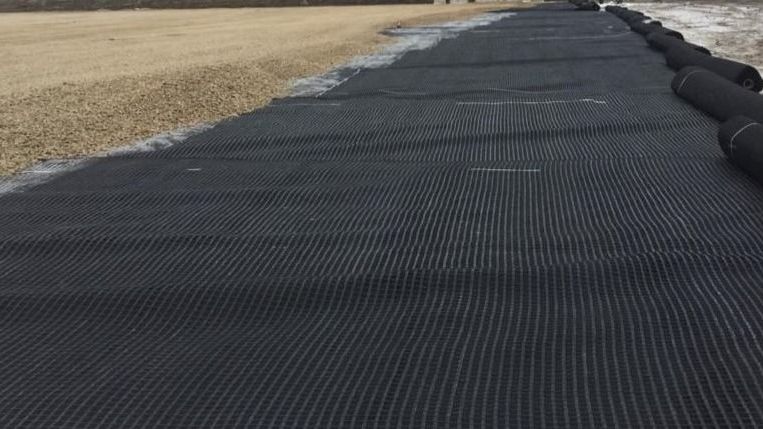Black silt fence lining a field edge beside a paved path under construction