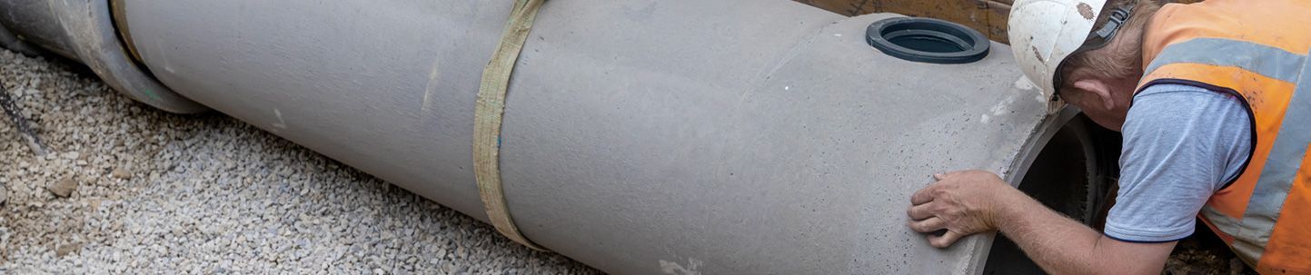 Worker rolls a large gray pipe into place outdoors