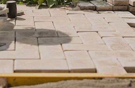 Stone patio under construction with light beige pavers and a yellow edge board
