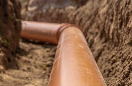 Rust-colored pipe running through a narrow dirt trench between rocky walls