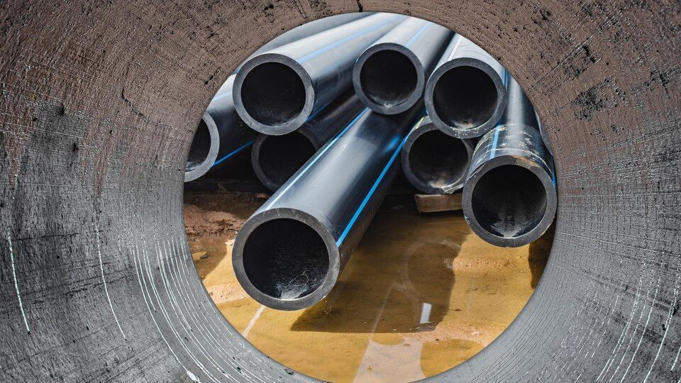 Stacked black pipes viewed through a concrete tunnel opening.