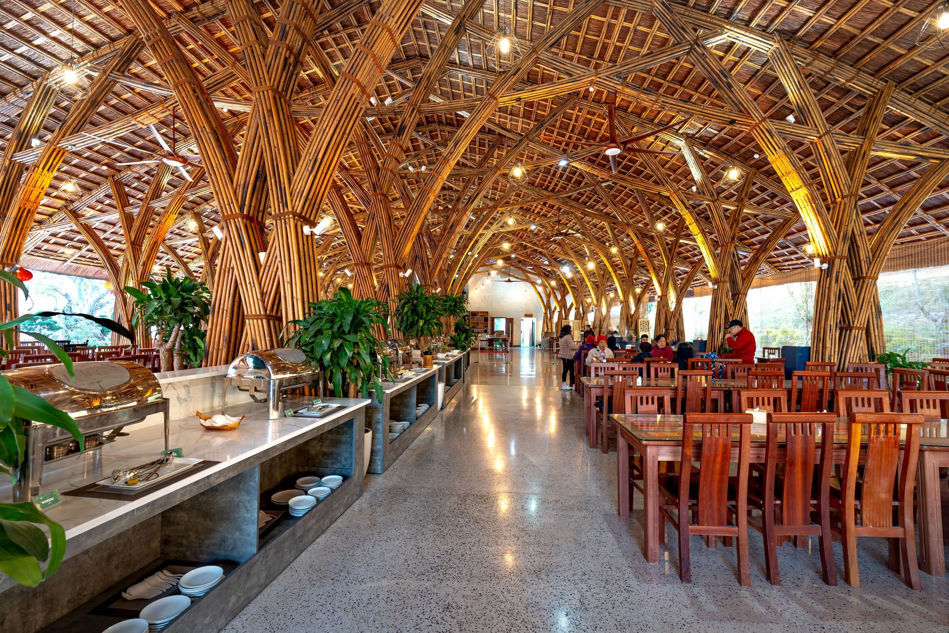 Open-air restaurant with woven bamboo arches, polished floor, and rows of wooden tables and chairs
