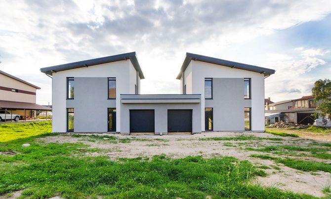 Modern two-story white house with a central garage, seen on a grassy lot under a cloudy sky