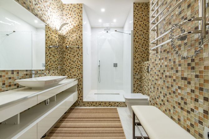 Modern bathroom with mosaic tile walls, glass shower, long vanity, and striped rug