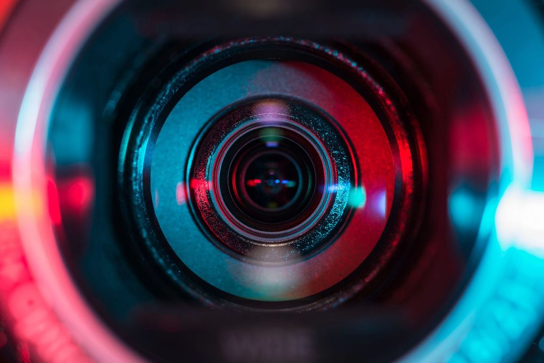 Primo piano di un obiettivo fotografico con riflessi al neon rossi e ciano.