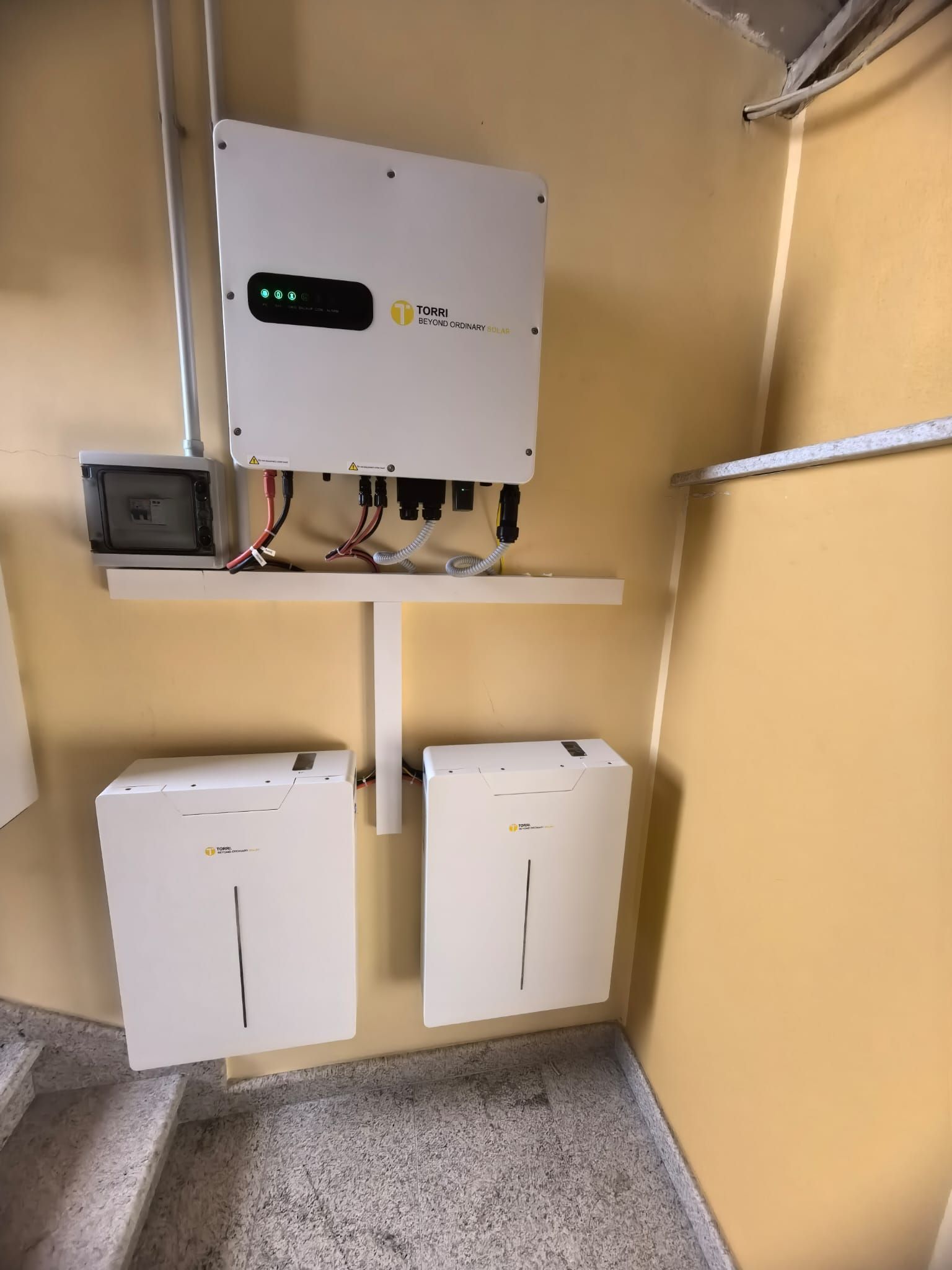 Quadri elettrici e inverter montati a parete in un locale tecnico beige con cavi e scaffalature a vista.