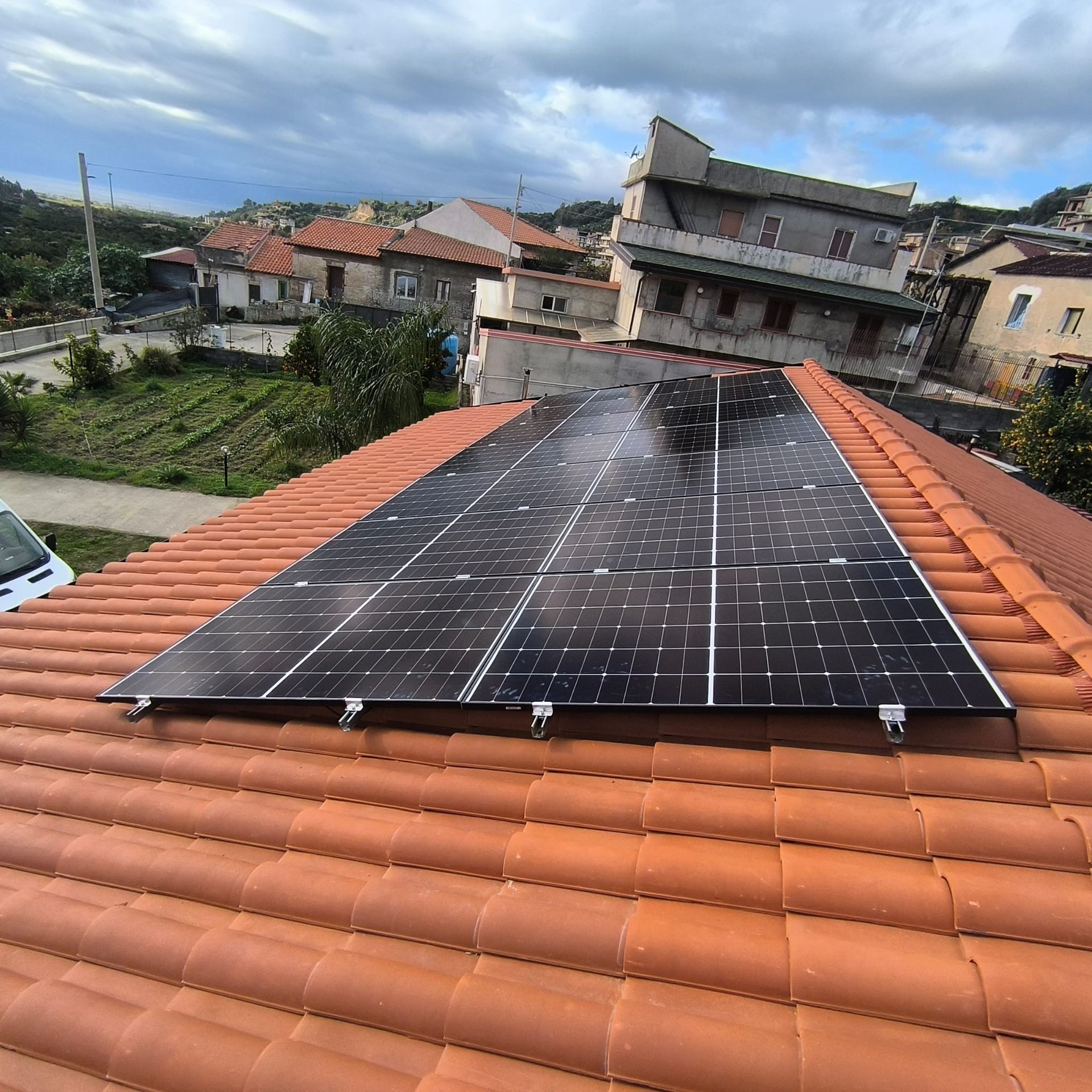 Pannelli solari installati su un tetto di tegole rosse in un quartiere residenziale, sotto un cielo nuvoloso.