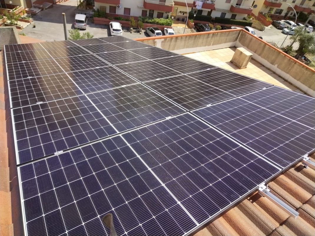 Un tetto ricoperto da file di pannelli solari blu, accanto a un tetto di tegole e alle case vicine.