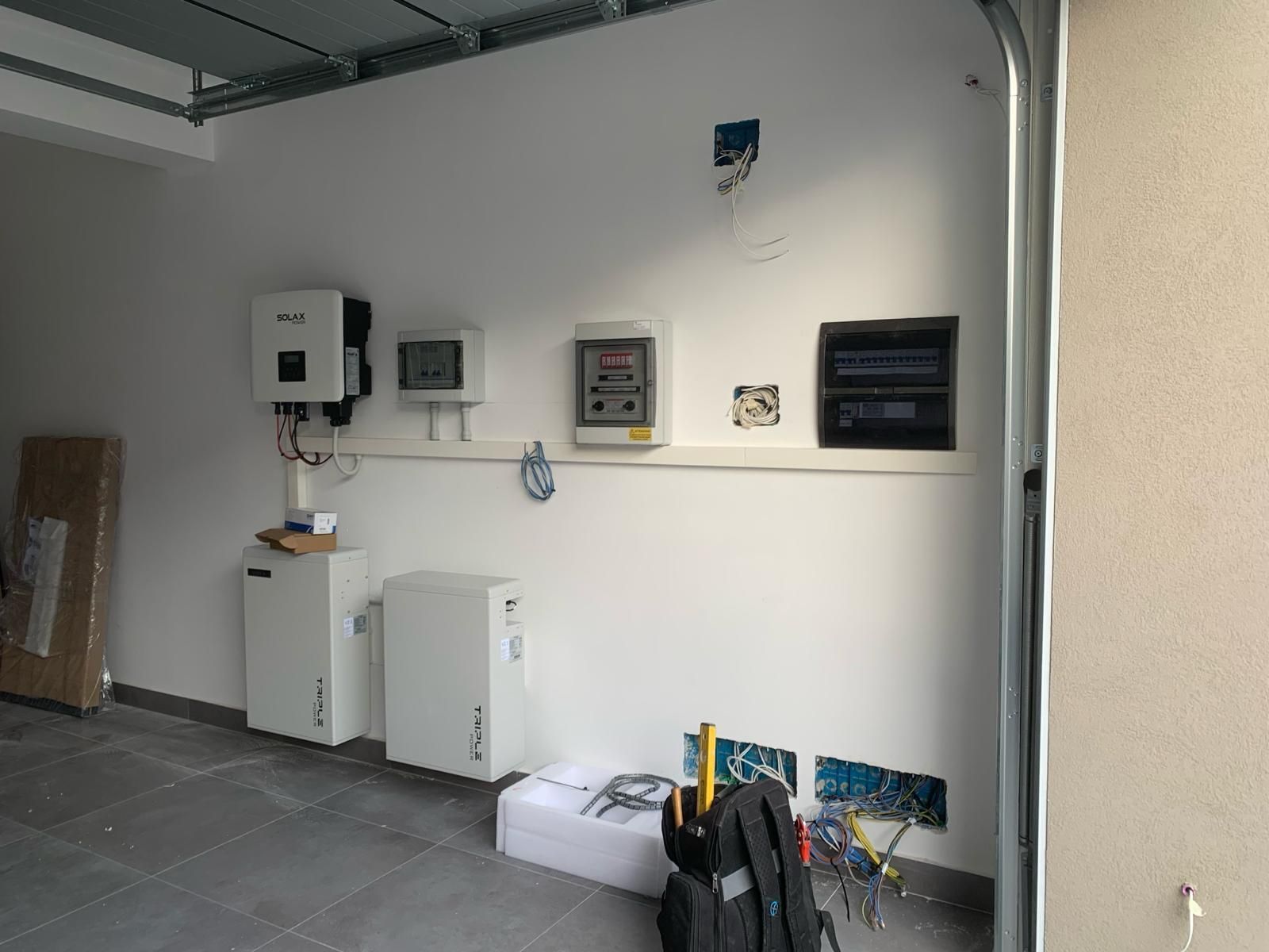 Parete del locale tecnico con pannelli elettrici, contatori e armadietti su un pavimento piastrellato.
