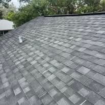 Roofer in yellow hard hat installing shingles on a sloped roof with a hammer