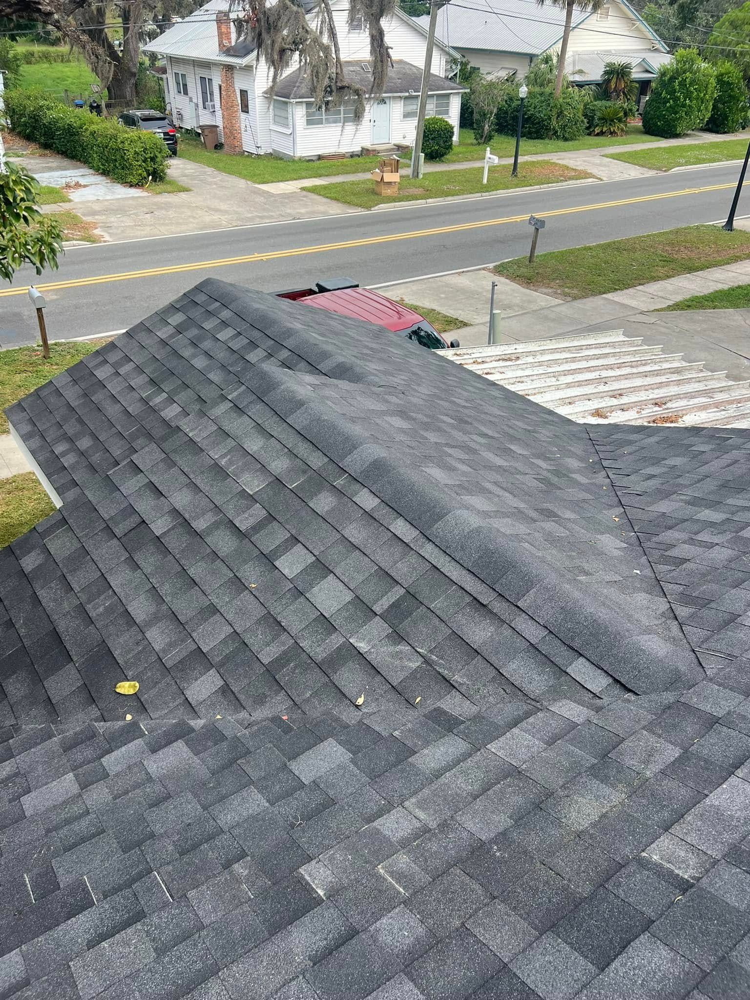 Dark gray shingled roof in foreground with a suburban street and houses in the background.