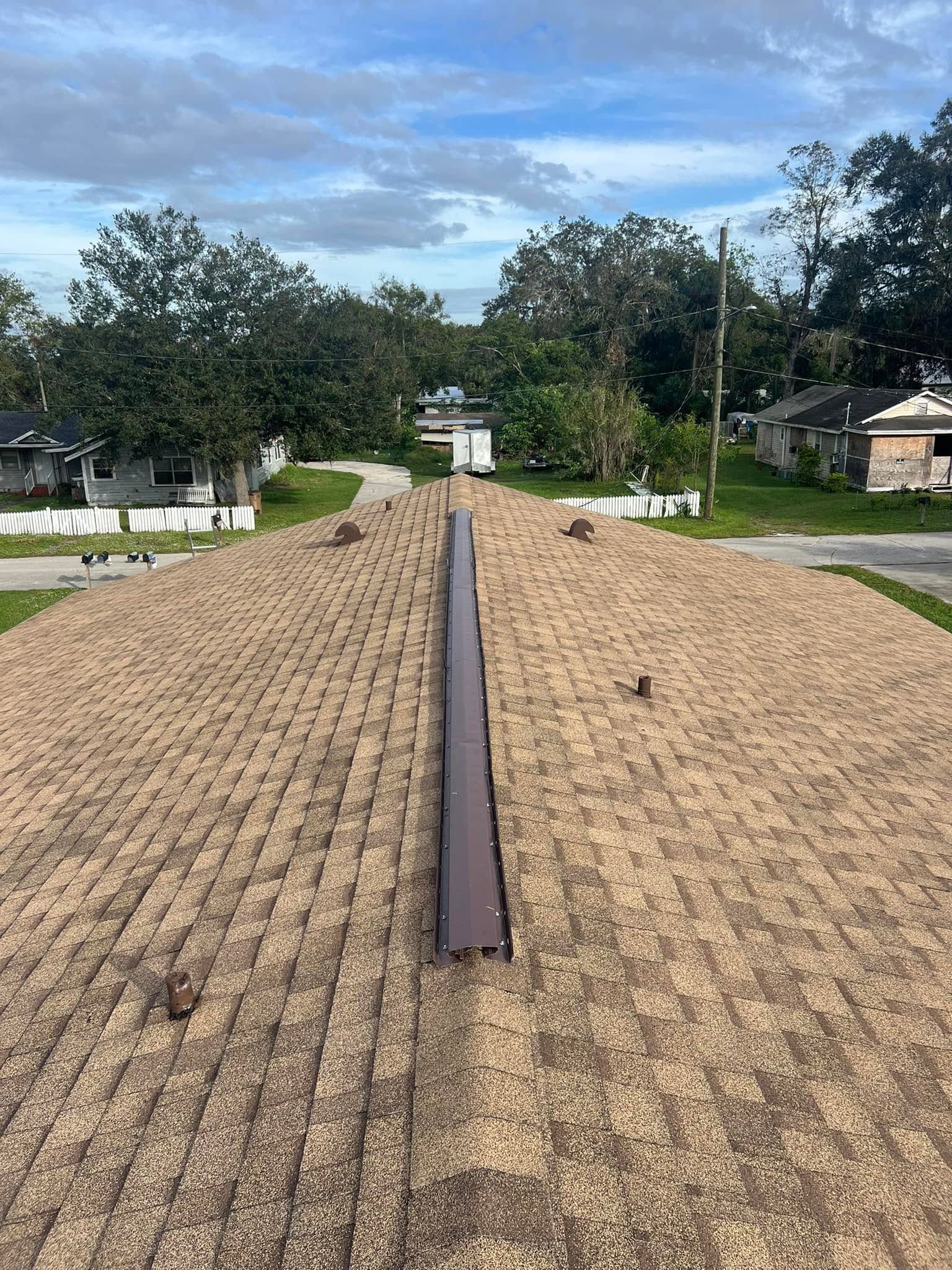 Long gravel path with a narrow central beam, flanked by trees and houses under a cloudy sky
