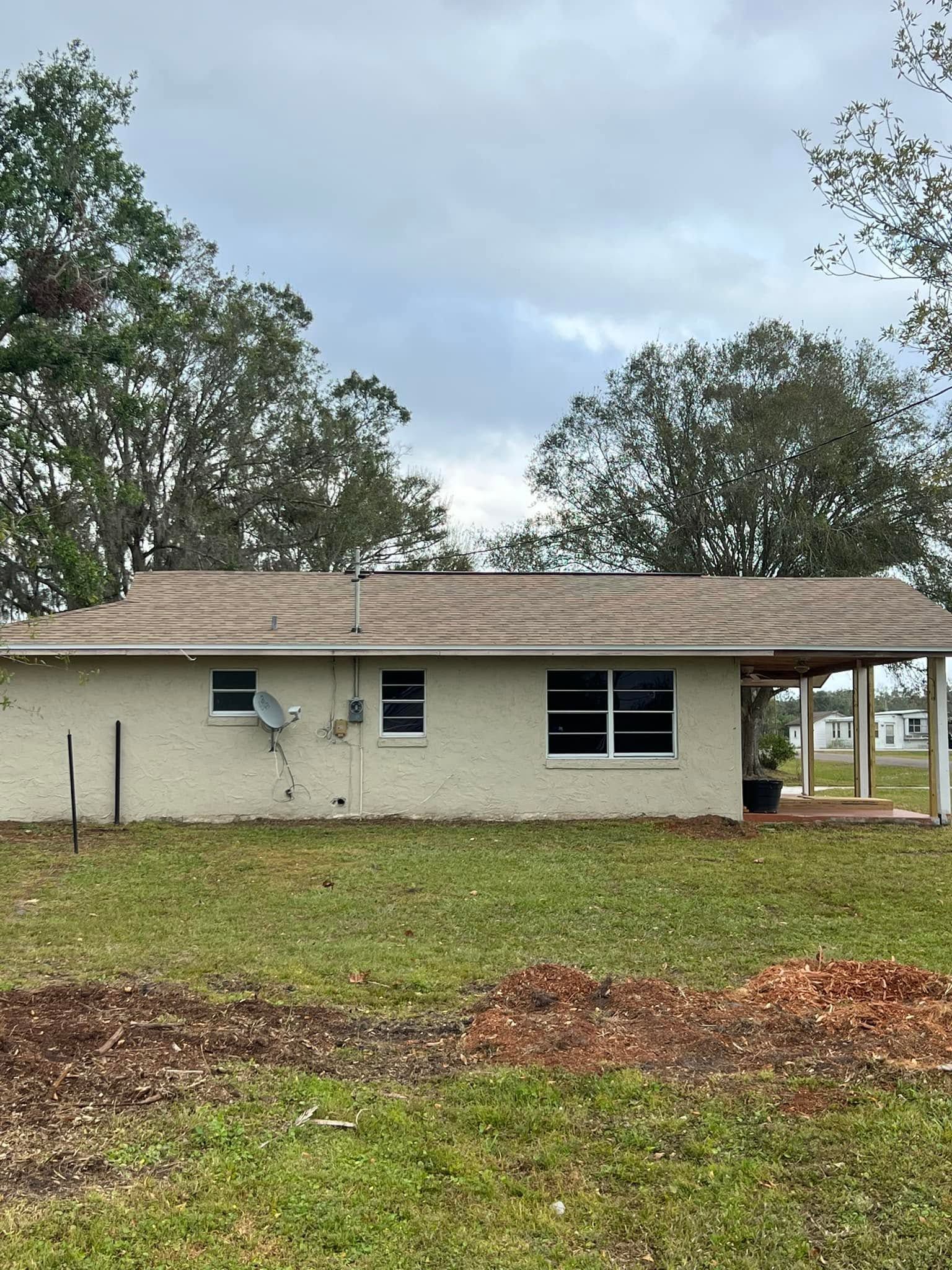 Single-story white house with a beige roof, front yard, and trees under a cloudy sky.