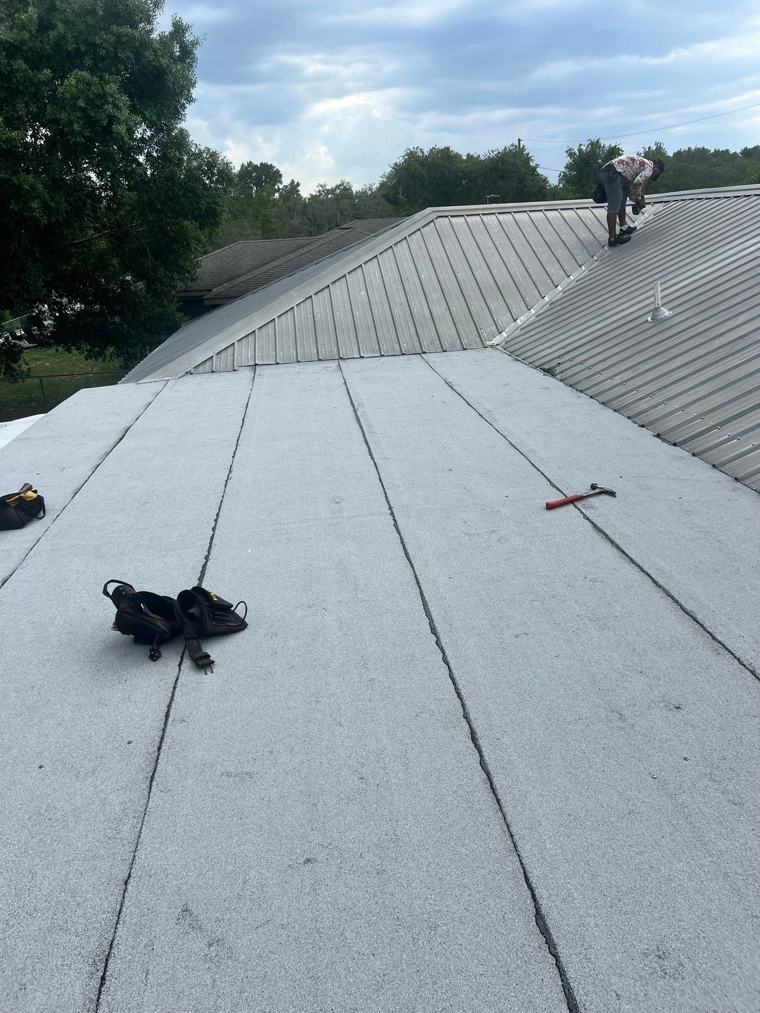 Roofers working on a gray shingled roof with trees in the background