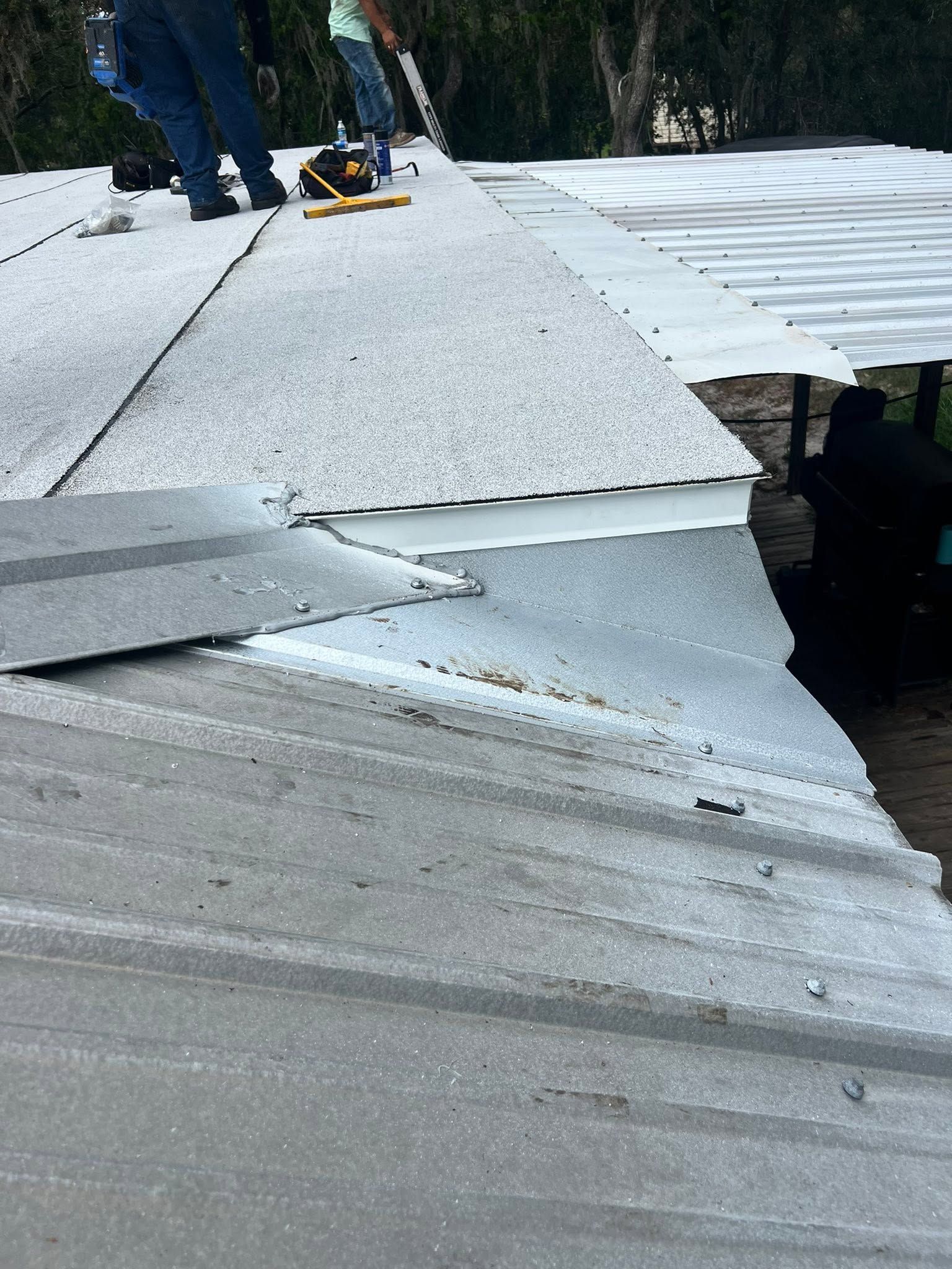 Damaged corrugated metal roof with bent, overlapping sheets and a person standing in the background.