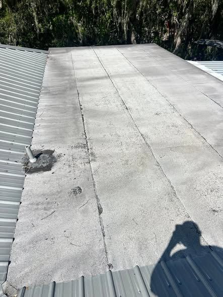 Flat gray roof with a metal edge, patches, and a small vent, viewed in bright sunlight.