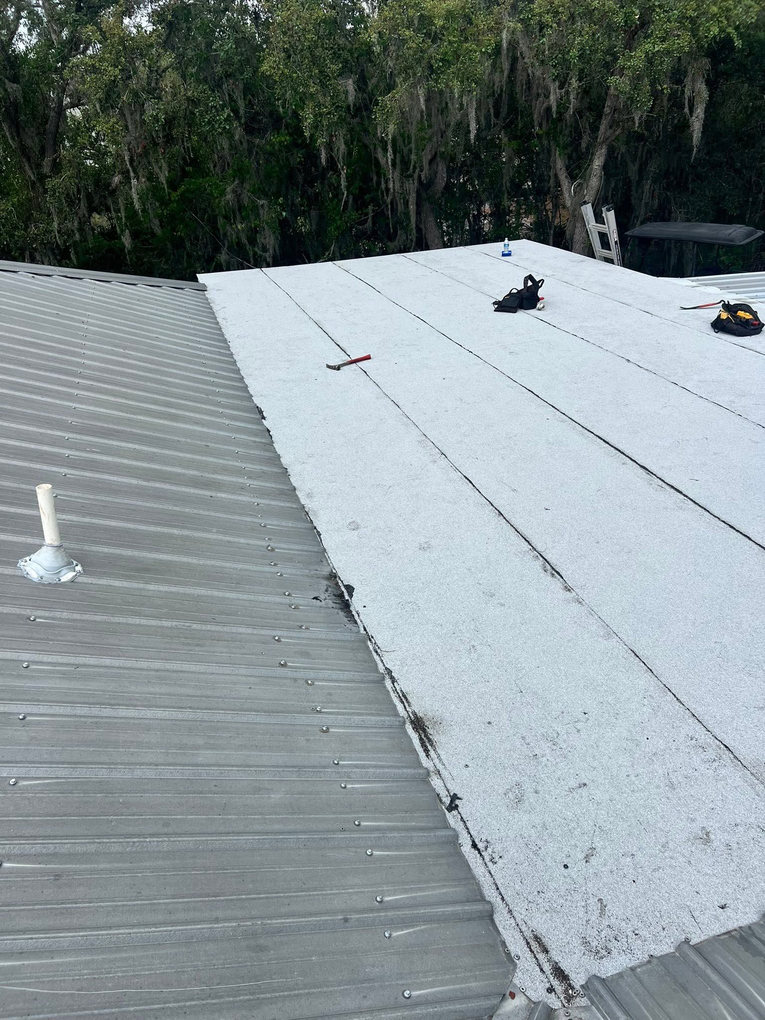 Two adjacent rooftop sections, one gray metal and one white coated, with trees in the background.