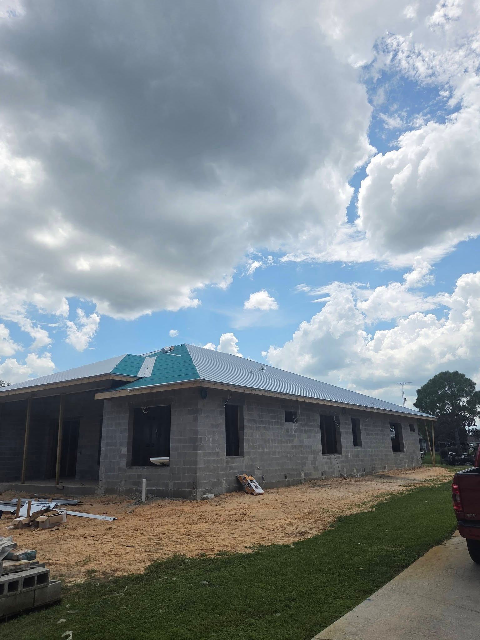 Partially built cinder block house with a blue metal roof under a cloudy sky