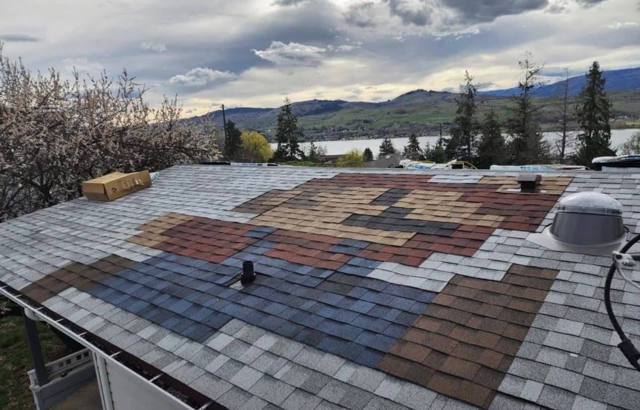 Damaged roof with patchwork shingles overlooking a lake and hills under cloudy skies