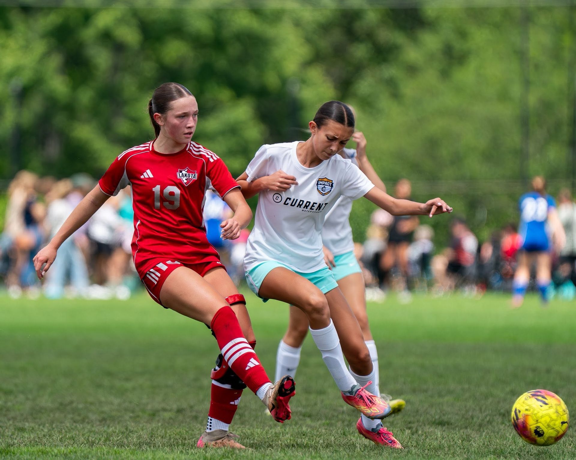 Two soccer players in red and white uniforms contest the ball on a grassy field