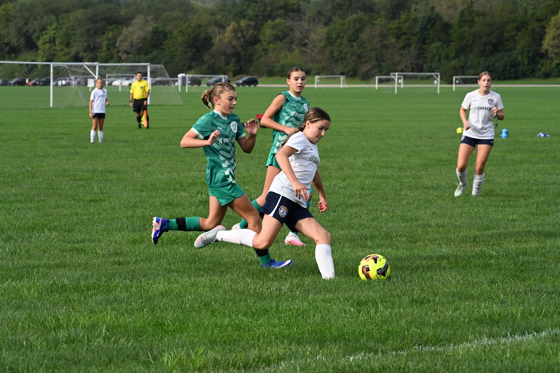 Youth soccer player in navy and white dribbles a ball on a rainy field during a match.