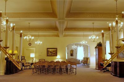 Elegant room with chandeliers, arched doorway, and rows of chairs, likely for a formal gathering.