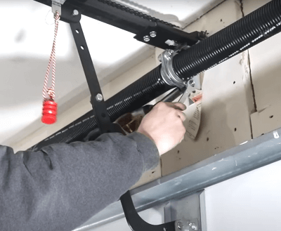 A man is fixing a garage door  spring with a wrench.