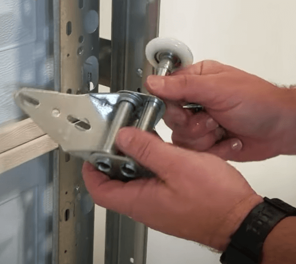 A person is holding a garage door hinge and inserting a roller into it. The roller glides up and down the tracks 